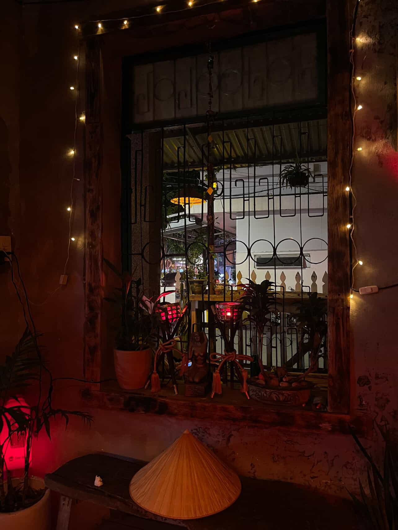 Window framed in fairy lights with a conical hat lamp and view through iron grillwork